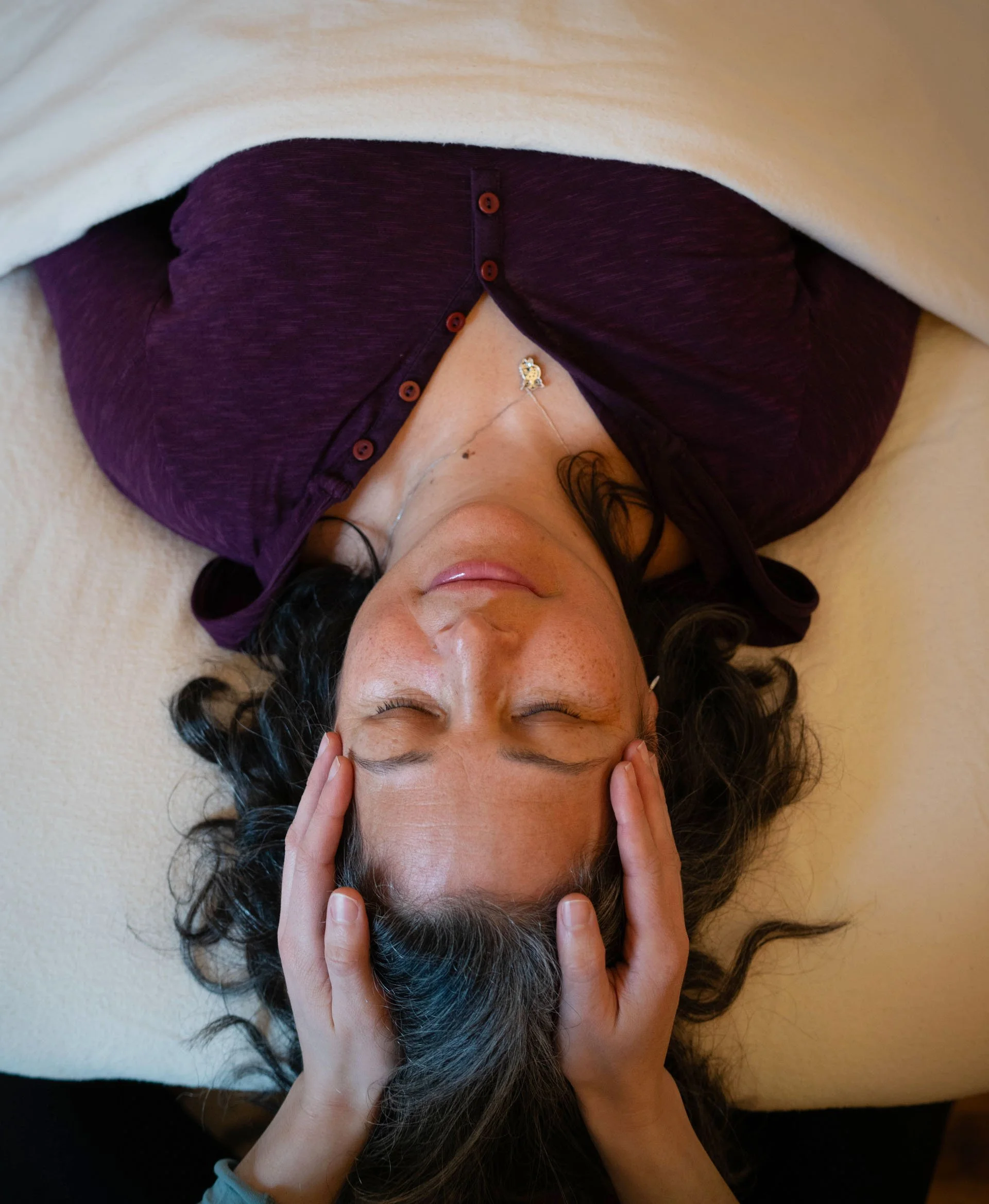 A client lying on the treatment table with eyes closed, Vanessa's hands cradling her head.