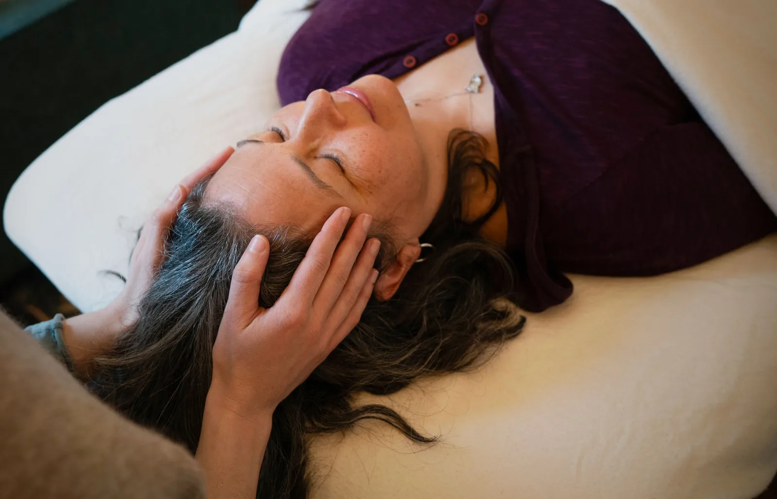 Vanessa holding a client's cranial vault during a craniosacral session, the client lying with eyes closed.