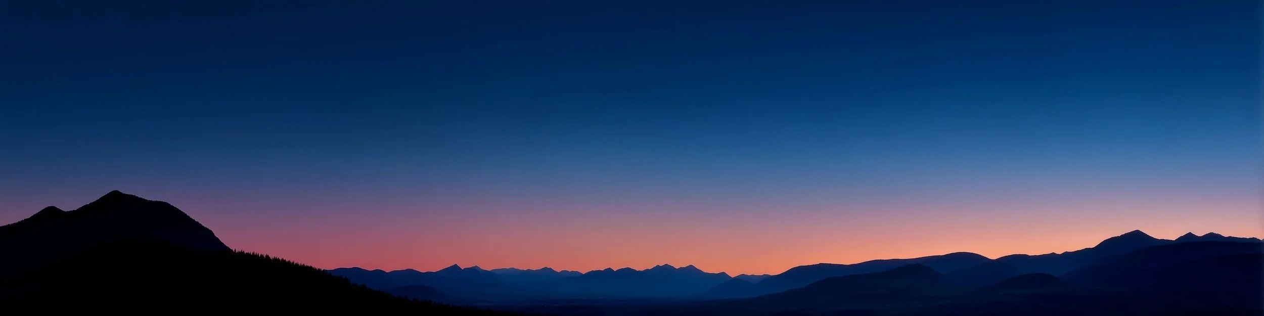 Silhouetted mountain ridges at dawn, the horizon glowing orange under a deep blue sky.