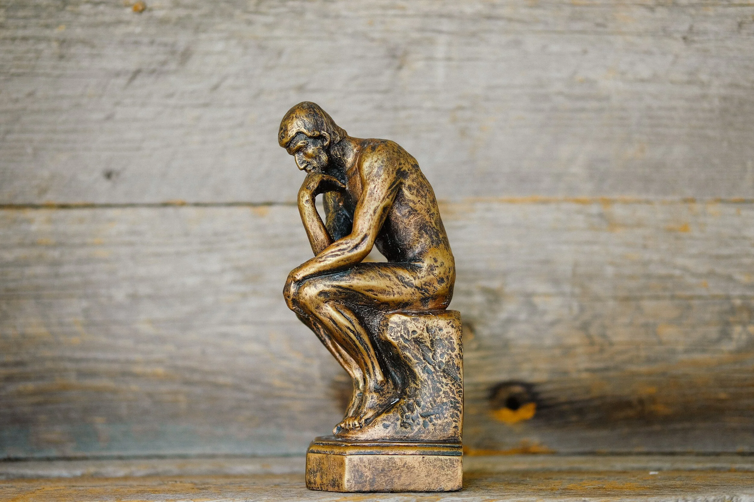 A small bronze figurine of Rodin's The Thinker on a weathered wooden shelf.