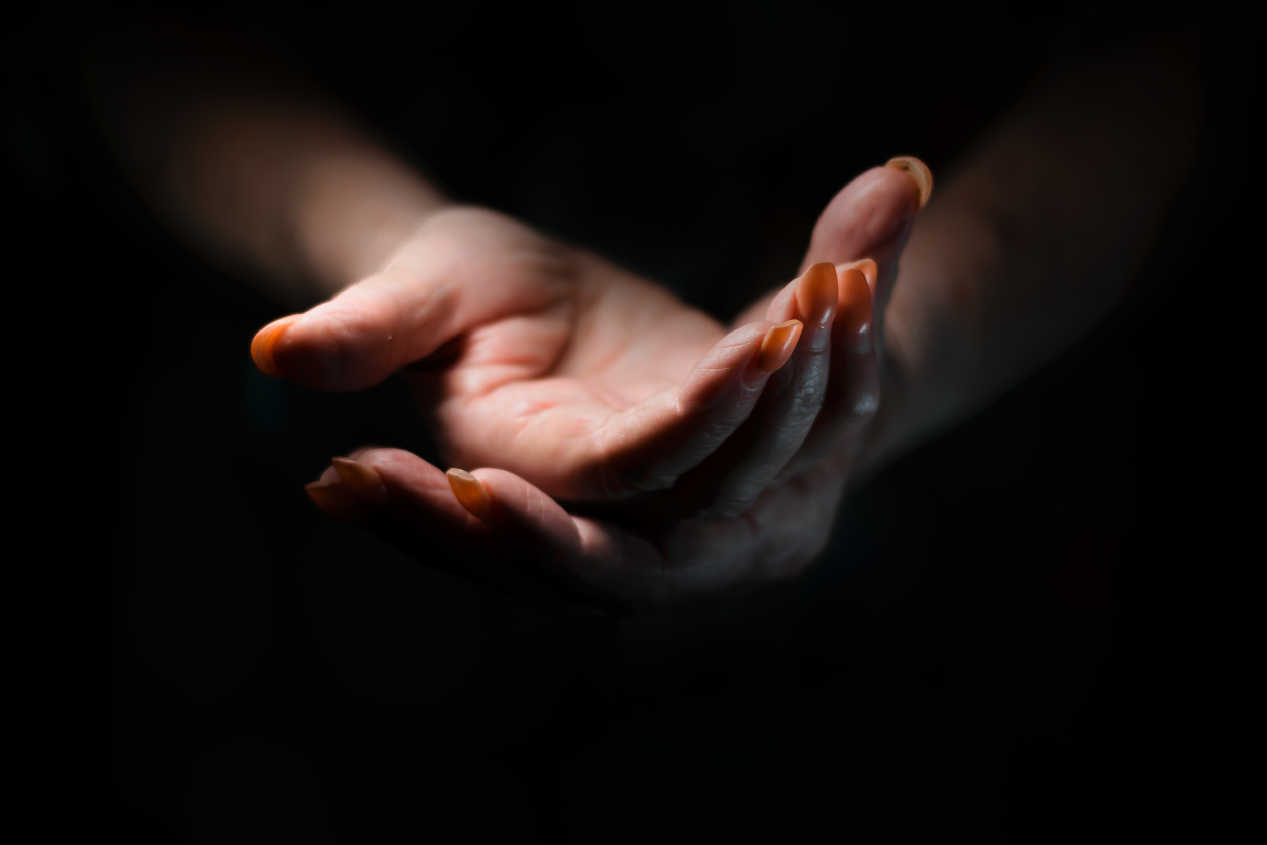 Two open hands, cupped and offered forward, lit against a dark background.