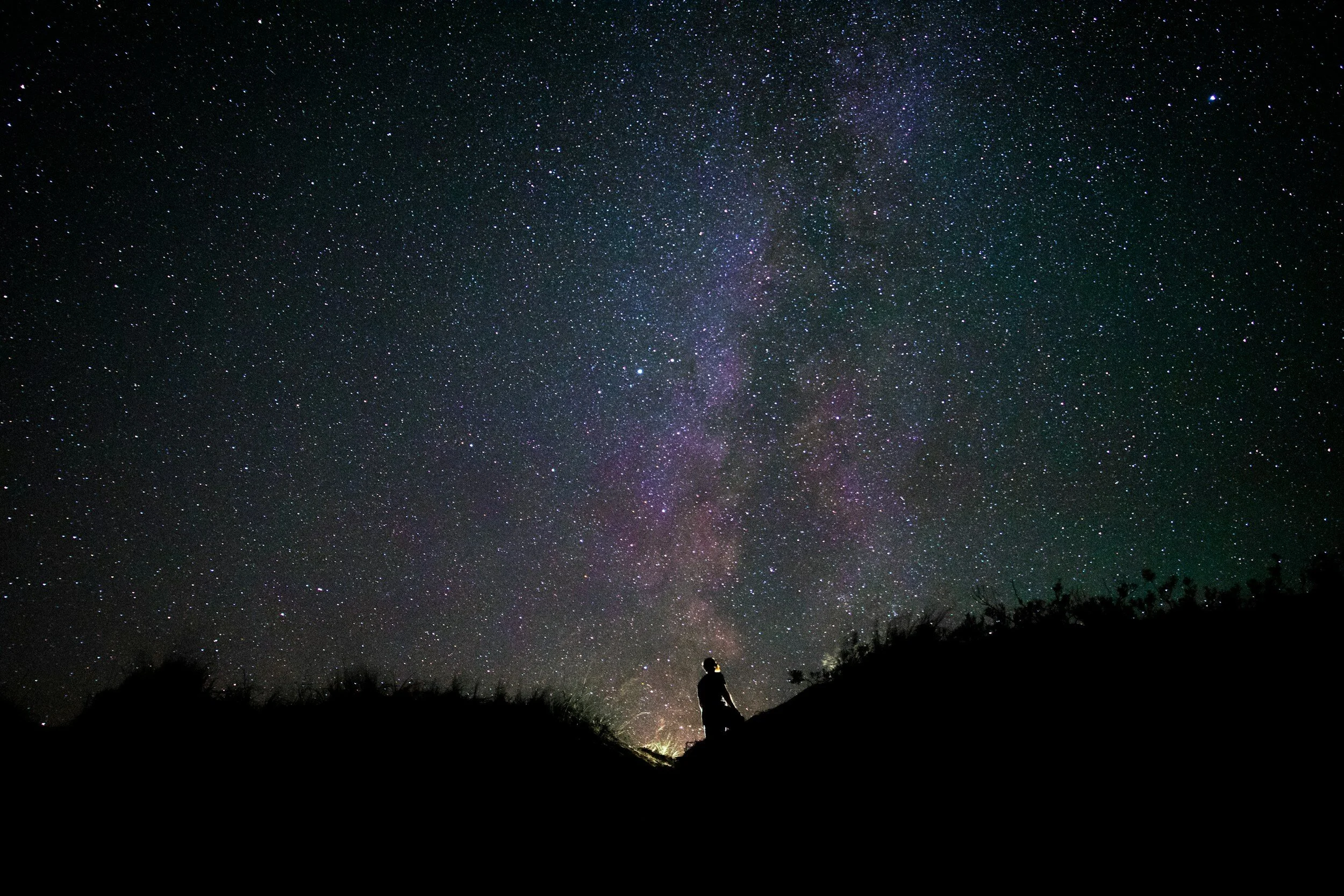 A person silhouetted on a hillside beneath the Milky Way.