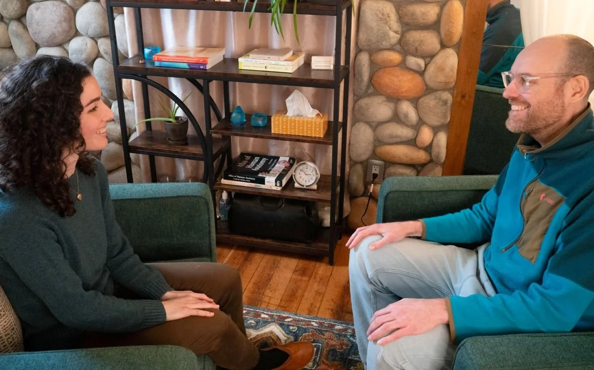 Vanessa and a client talking in her office, seated in green armchairs beside a bookshelf.