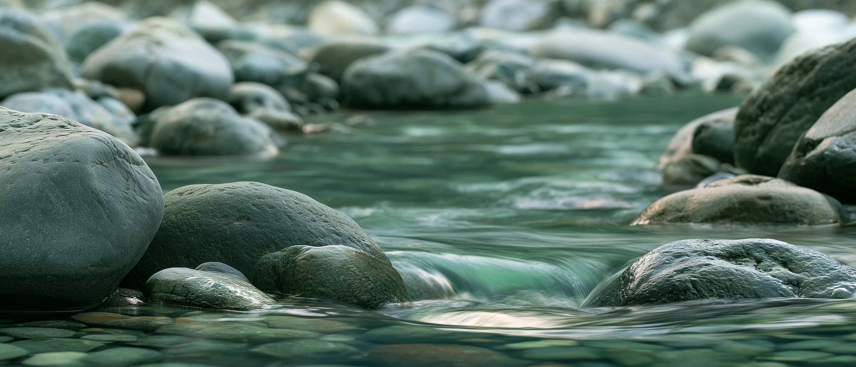 A clear stream flowing between smooth grey-green stones.