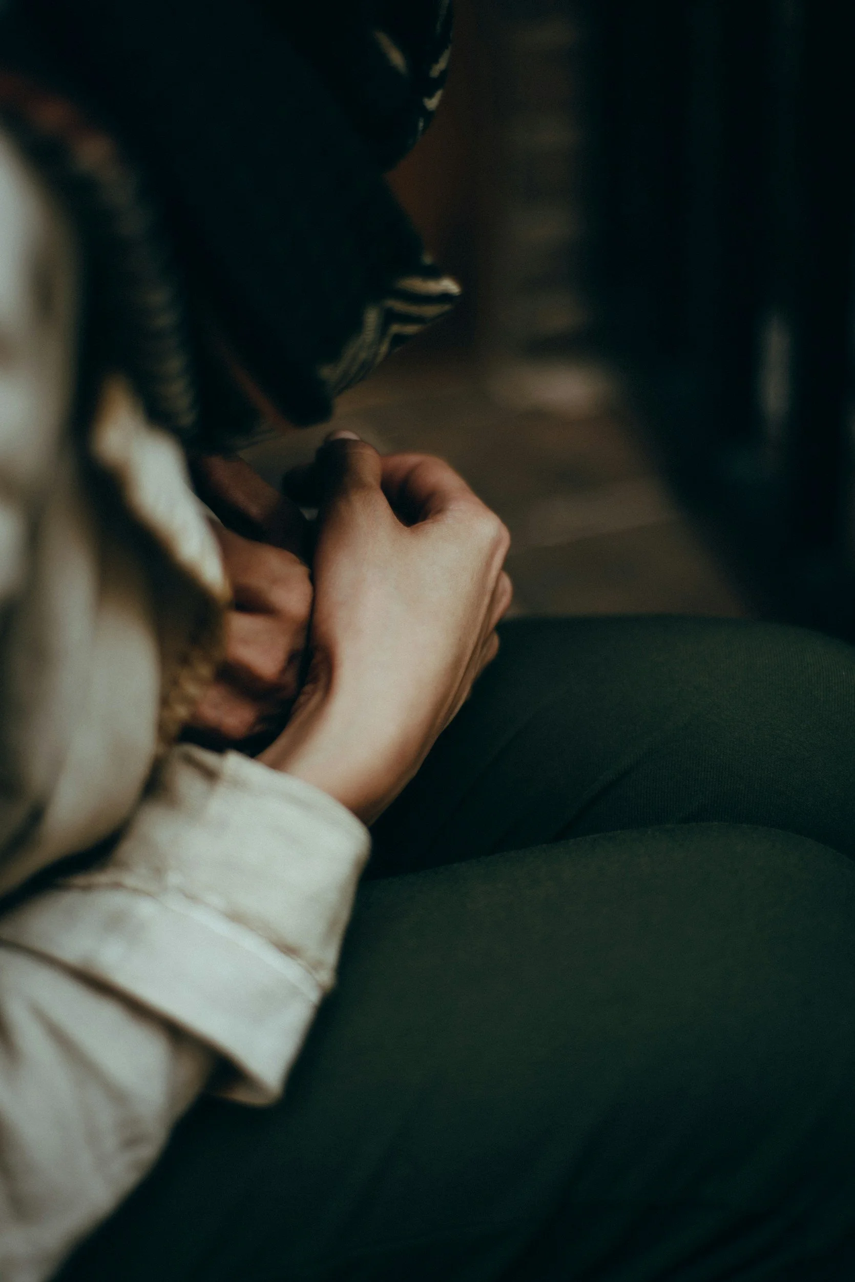 A seated person seen from above, hands clasped in their lap.