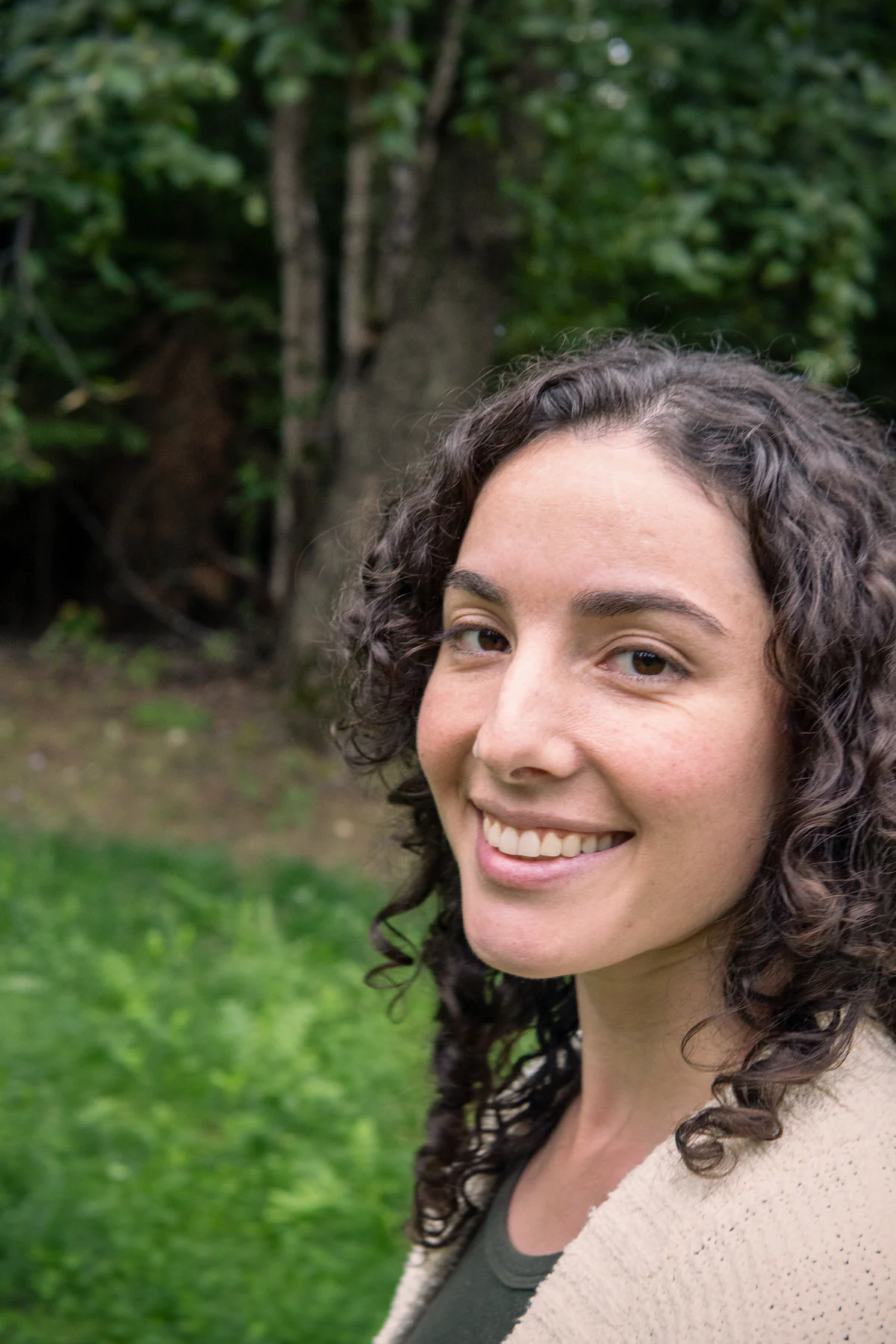 Vanessa Deverell smiling, close up, among green trees near Nelson, BC.